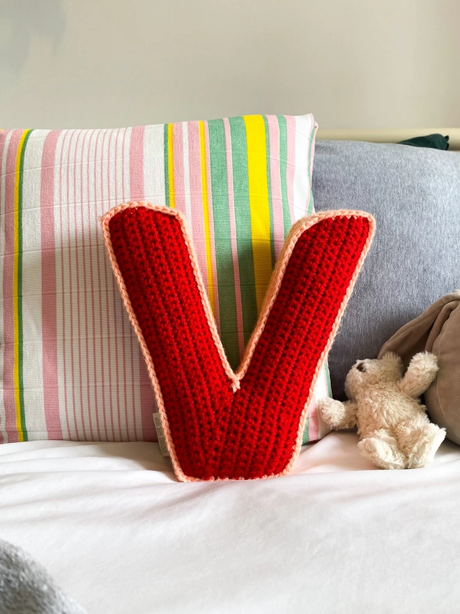 V shaped crochet cushion in Red and Peachy Pink, on a bed