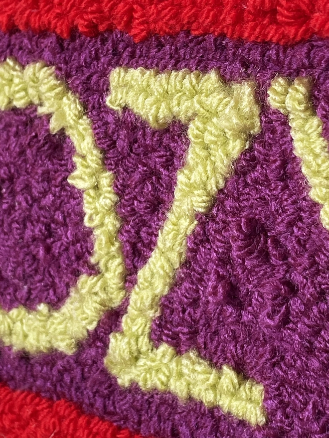 lime green o and z in punch needle wool loops on purple wool loops with red edge
