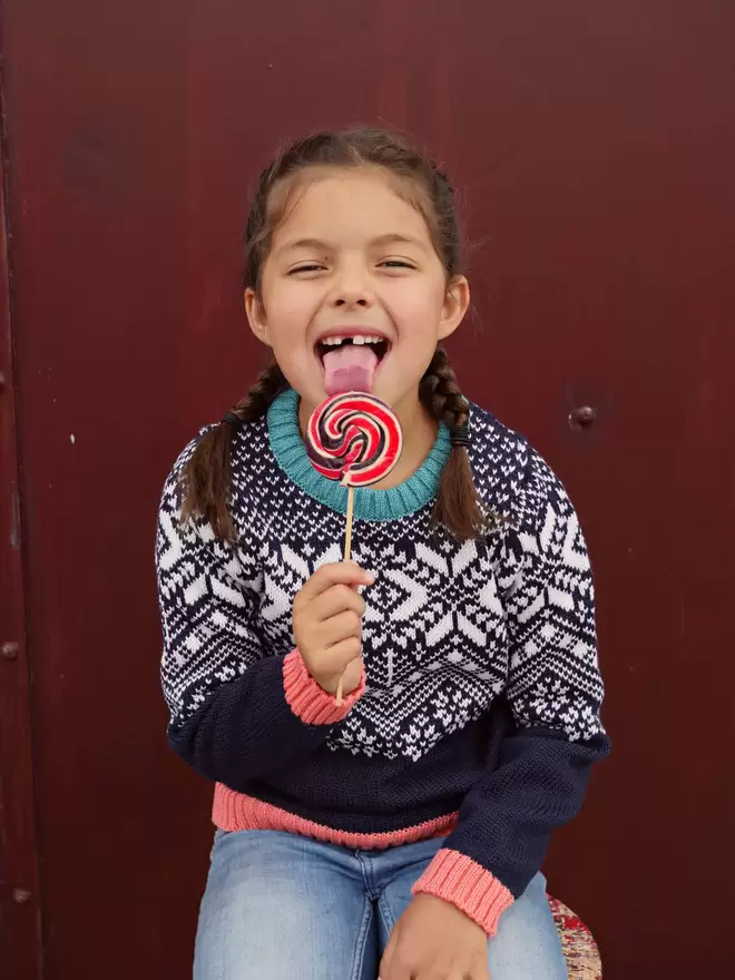 A girl in pigtails wearing the navy storyteller and licking a lollypop.