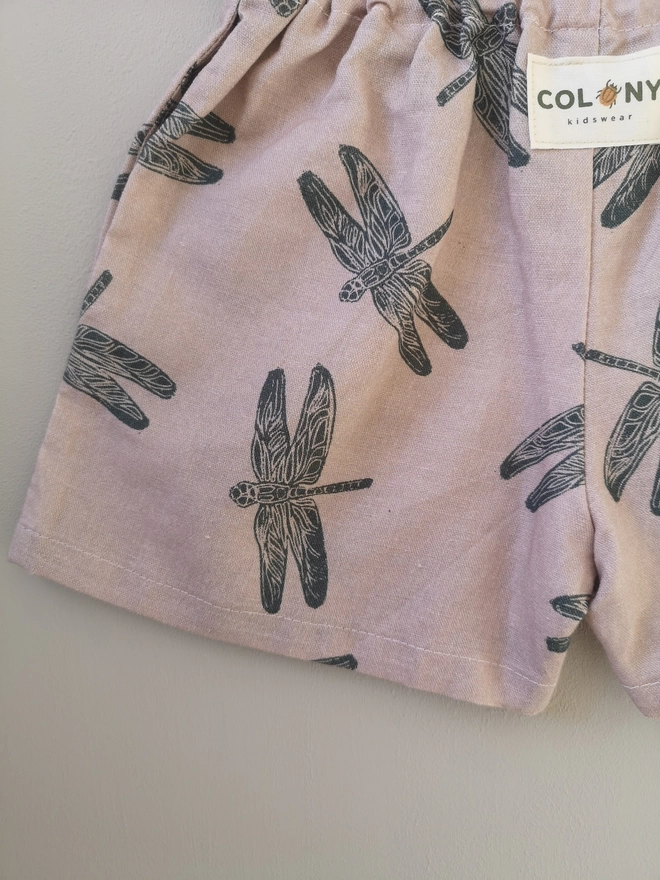 Pink cotton linen lightweight unisex childrens shorts. Featuring a delicate grey dragonfly print. Simple design with elasticated waist and side seam pockets. 