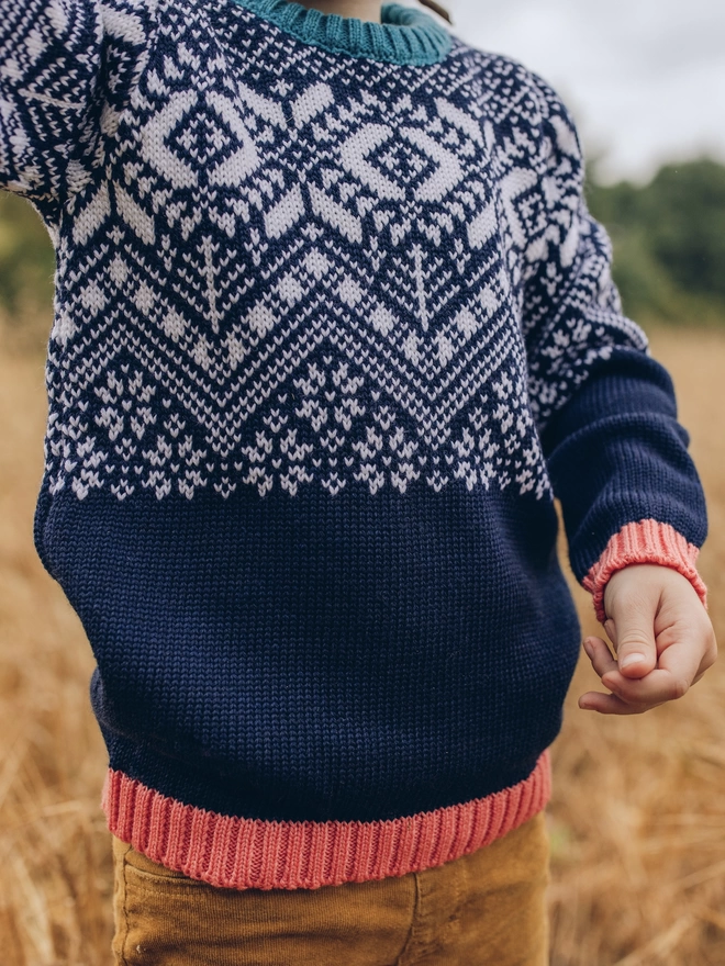 A child standing in a field wearing The Faraway Gang's 'Storyteller' Jumper.
