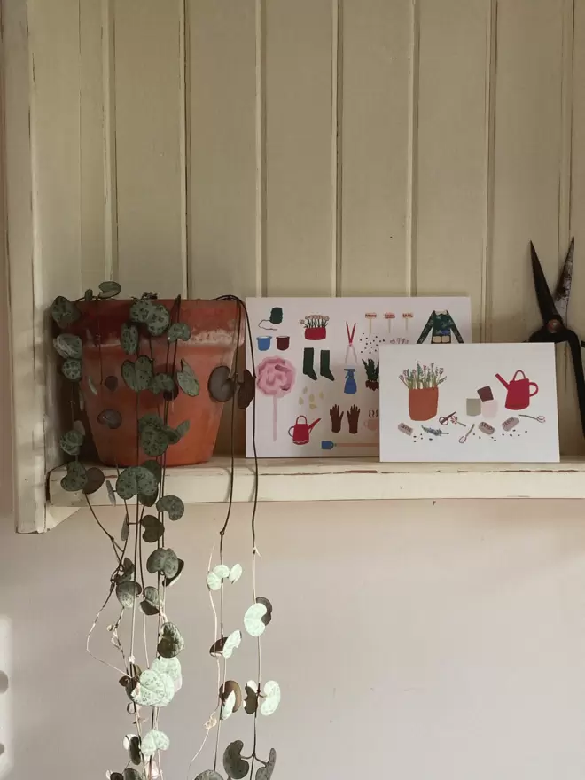 2 gardening greetings card on a white shelf next to plant