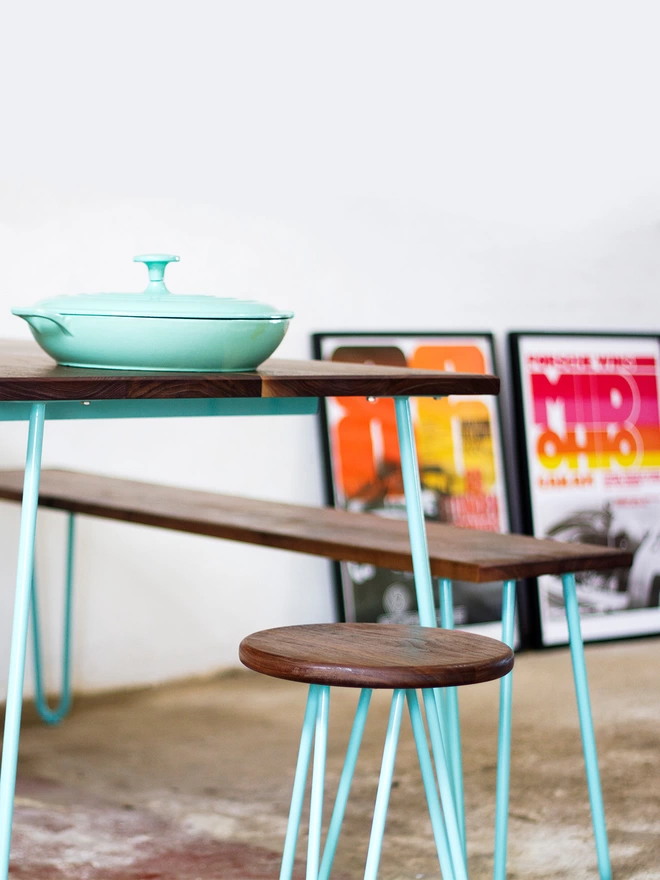 end view of a hairpin leg dining set with a bench on one side and a stool at the end, all with walnut wood tops and turquoise hairpin legs