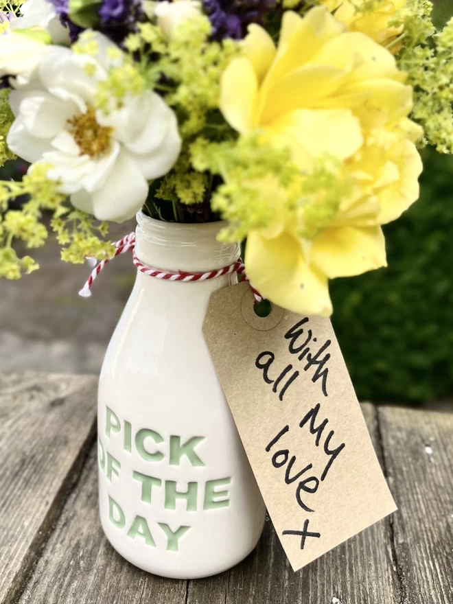 A handmade ‘pick of the day’ bottle/vase is filled with flowers, with a thank you note tied to its neck. 