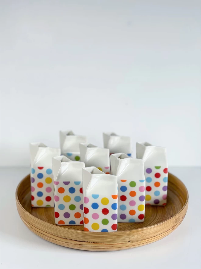 Group of eight colorful polka-dot porcelain milk carton jugs on a round bamboo tray
