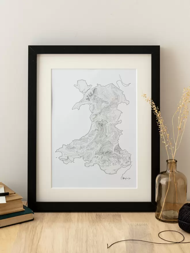 Print of a detailed pen and watercolour drawing of the map of Wales showing contour lines, in a soft white mount and black frame