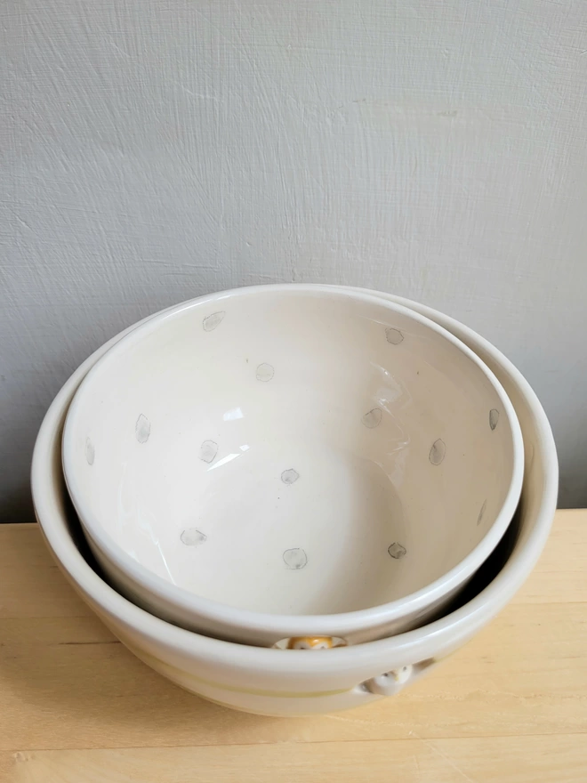 2 ceramic cream bowls stacked with the smaller grey and white spotty bowl inside the larger bowl on a wooden counter